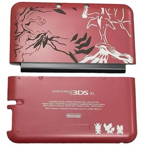 Op de afbeelding: Een rode Nintendo 3DS XL handheld gameconsole. De bovenklep heeft een zwart-wit grafisch ontwerp. De onderste klep heeft de tekst "NINTENDO 3DS XL" en het Nintendo-logo. Bevat de tekst: "©2013 Pokémon. ©1995-2013 Nintendo/Creatures Inc./GAME FREAK inc."