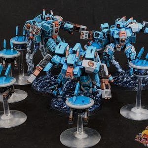 Puede incluir: Una colección de robots y drones en miniatura, detallados, azules y naranjas. Los robots tienen extremidades y armas articuladas, y están colocados sobre una base texturizada de color azul oscuro. Los drones son pequeños, con una parte superior circular y están sostenidos por soportes transparentes.