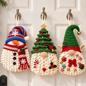 Könnte beinhalten: Drei gehäkelte Wandbehänge für die Feiertage, bestehend aus einem Schneemann mit blau gestreifter Mütze, einem Wichtel mit grünem Weihnachtsbaum-Hut und einem Elf mit grüner Zipfelmütze, jeweils mit strukturiertem weißem Bart und Verzierungen.