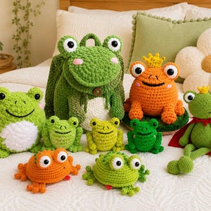 Könnte beinhalten: Eine Sammlung handgefertigter Häkel-Frosch-Artikel, darunter ein großer grüner Rucksack, ein orangefarbener Plüschfrosch mit gelber Krone, ein grüner Frosch mit rotem Umhang und gelber Krone sowie mehrere kleinere grüne und orangefarbene Plüschfrösche.