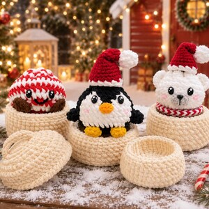 Könnte beinhalten: Drei gehäkelte Plüschfiguren, darunter ein rot-weißer Pfefferminzbonbon, ein schwarz-weißer Pinguin und ein weißer Eisbär, die jeweils eine rot-weiße Weihnachtsmütze tragen und in cremefarbenen Häkelkörben sitzen, wobei einer leer ist.