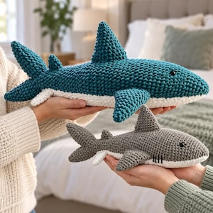 May include: Two handmade crochet shark plushies, one larger teal shark and one smaller grey shark. Both sharks feature a textured yarn finish, a white underbelly, a dorsal fin, pectoral fins, and a tail. Each shark has a small black bead eye.