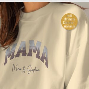 Puede incluir: Sudadera color crema con la palabra "MAMA" en una fuente retro en capas. Debajo de la palabra "MAMA" están los nombres "Max & Sophie" en una fuente de escritura. Un adhesivo dorado a la derecha dice "mit deinen Kindernamen".