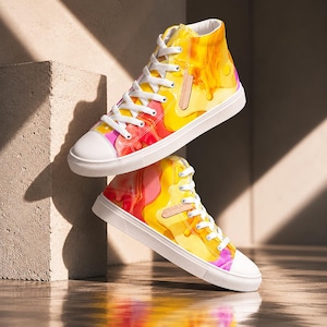May include: High-top sneakers with a vibrant, abstract design in shades of yellow, orange, and pink. The shoes have white laces, a white toe cap, and a white sole. A small, tan leather-like accent is on the side of each shoe.