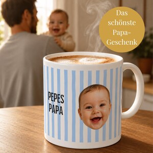 Pode incluir: Uma caneca de cerâmica branca com riscas verticais azul-claras, o texto "PEPES PAPA" a preto e uma impressão fotográfica do rosto de um bebé a sorrir. A caneca contém uma bebida quente com vapor visível na parte superior.