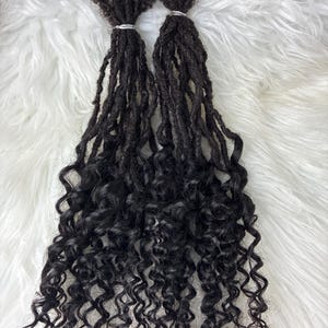 May include: A set of dark brown hair extensions featuring a textured, matted root section that transitions into long, loose, spiral curls. The hair strands are bundled together at the top with a small, thin, silver-colored metal band.