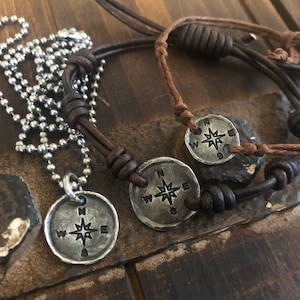 Puede incluir: Dos collares de cord&oacute;n de cuero con colgantes de br&uacute;jula. Los colgantes son de plata y presentan una rosa de los vientos con las letras N, S, E y W.