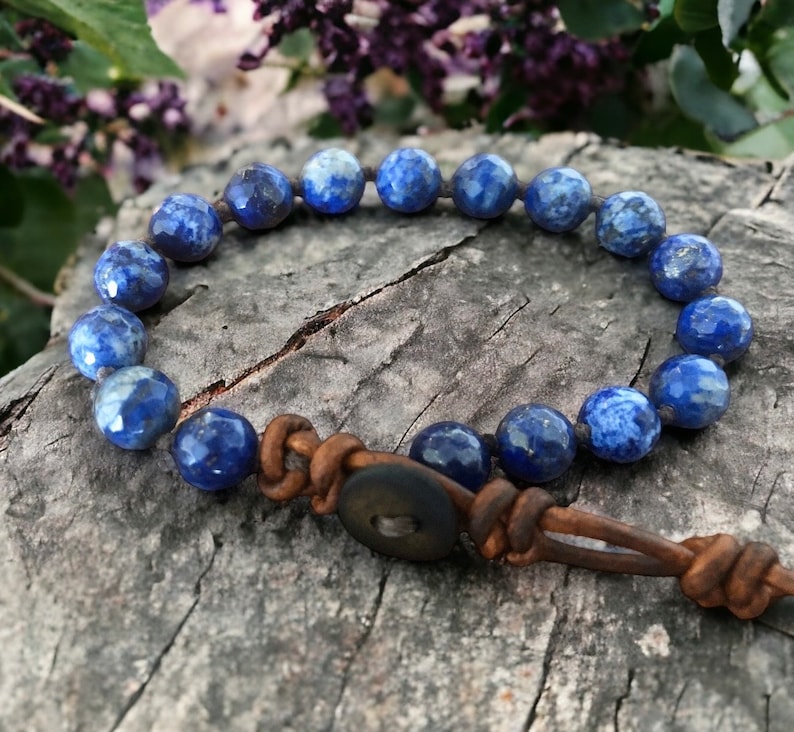 K&ouml;nnte beinhalten: Ein blaues Lapislazuli-Perlenarmband mit einem braunen Lederband und einem Holz-Knopfverschluss.