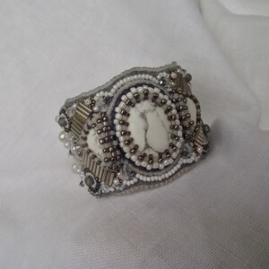 May include: A white stone bracelet with silver and gray beads. The bracelet is beaded with a circular design and a large white stone in the center.