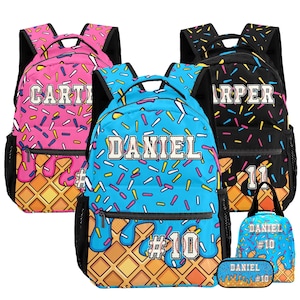 May include: Three backpacks in pink, blue, and black, each featuring a waffle cone base, melting icing, and colorful sprinkles. The backpacks are personalized with names like Carter, Daniel, and Harper, plus jersey-style numbers. Includes a matching lunch bag and pencil case.