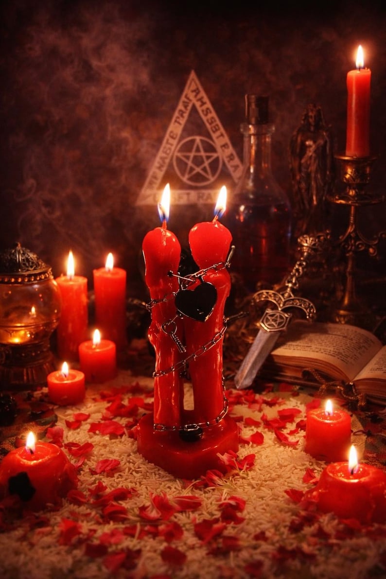 May include: A mystical scene featuring red candles of various sizes, some adorned with chains and a black heart-shaped lock. A pentagram symbol is visible in the background, along with a decorative sword and an open book. The scene is illuminated by candlelight and scattered rose petals.