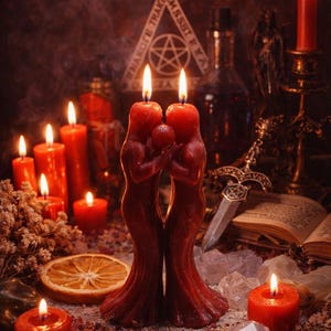 May include: A mystical scene featuring burning red candles of various sizes, including two figure-shaped candles embracing a sphere. Other elements include a dagger, crystals, and an open book, creating a gothic or Wiccan aesthetic.