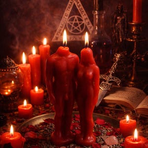 May include: A mystical scene featuring red candles of various sizes, including two figure-shaped candles. The candles are arranged on a tray with rose petals and crystals. Other items include a book, a dagger, and a bottle.