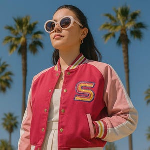 May include: A pink and red letterman jacket with a large embroidered "S" on the front. The jacket has light pink sleeves and white trim. The person is wearing light pink sunglasses.