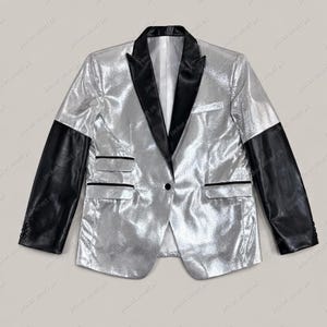May include: Silver blazer with black leather sleeves and a black lapel. The jacket has a single-button closure and two front pockets. The jacket is a unique and stylish piece of outerwear.