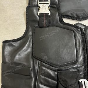 Op de afbeelding: Zwart leren vest met meerdere zakken en een ritssluiting aan de voorkant. Het vest heeft een zilveren gespsluiting en de tekst "JACKETSMART" is zichtbaar.