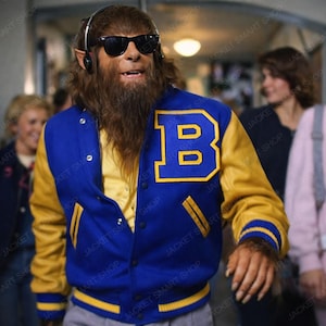 May include: A blue and yellow varsity jacket with a large letter "B" on the chest. The jacket has yellow sleeves and trim, with a snap-button closure. The image is from Jacket Smart Shop.