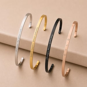 Pode incluir: Quatro pulseiras de metal em tons de prata, ouro, preto e ouro rosa. A pulseira prateada tem gravado "Forever by your side", a dourada "Make it happen. Shock everyone", a preta "Stronger than yesterday" e a de ouro rosa tem símbolos de sol, lua e estrelas.