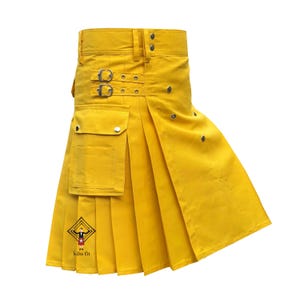 Può includere: Un kilt utilitario giallo brillante caratterizzato da un'ampia fascia in vita con passanti, due cinghie laterali regolabili con fibbie in metallo e una grande tasca cargo frontale. Il capo presenta pieghe verticali e il logo Kilts fit.
