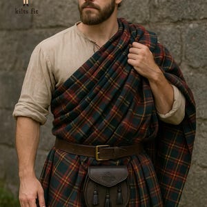 Op de afbeelding: Een beige shirt met lange mouwen gecombineerd met een kilt en schouderdoek in een donkergroen, rood en geel ruitpatroon. Een bruine leren riem met een koperen gesp houdt een donkerbruine leren sporran vast met drie kwastjes en reliëf.