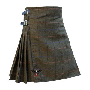 Może przedstawiać: Zielony kilt z kratą z czerwonych i niebieskich linii. Kilt ma dwa czarne skórzane paski ze srebrnymi klamrami. Na dole kiltu znajduje się mały haftowany obrazek osoby w kilcie z napisem "Kilt Fit".