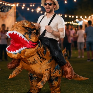 May include: An inflatable brown and black Tyrannosaurus Rex costume with a wide-open mouth showing white teeth and a red interior. The costume features a saddle-like design with black straps, allowing the wearer to appear as if riding the dinosaur.