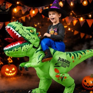 May include: An inflatable green T-Rex dinosaur costume featuring a wide-open mouth with white teeth and a red tongue. The side of the dinosaur body displays the text JURASSIC and additional lettering. The costume is worn with a black witch hat.