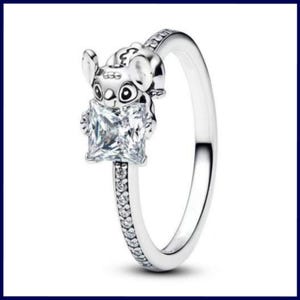 May include: A silver ring featuring a cartoon character holding a square, clear gemstone. The ring band is embellished with small, clear stones. The character has large eyes and ears. The ring is set against a white background.