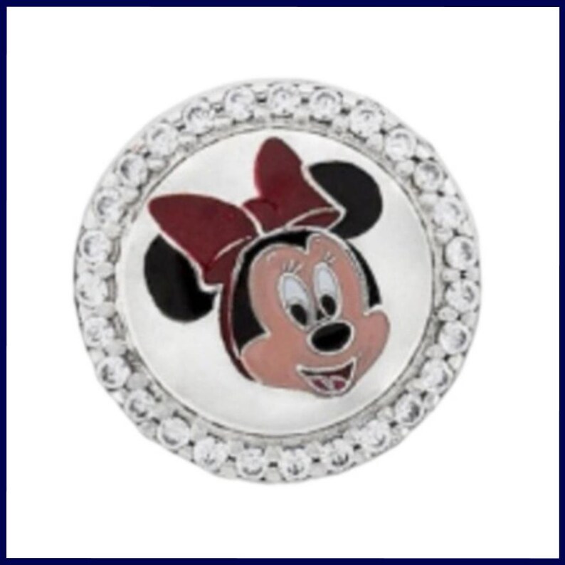 K&ouml;nnte beinhalten: Ein runder, silberfarbener Charm-Anh&auml;nger mit einem Cartoon-Bild von Minnie Mouse. Das Design zeigt Minnie's Gesicht in Rosa, Schwarz und Rot auf wei&szlig;em Hintergrund. Der Rand ist mit kleinen, klaren Kristallen besetzt.