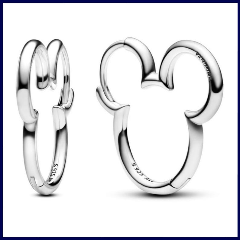 Op de afbeelding: Een paar zilveren oorringen. E&eacute;n oorring is een klassiek ontwerp, terwijl de andere de vorm heeft van Mickey Mouses hoofd. De oorbellen zijn gemarkeerd met "S925 ALE" en het Pandora-logo. De oorbellen zijn gemaakt van glanzend, reflecterend metaal.