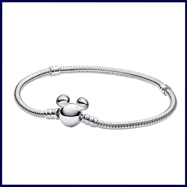 K&ouml;nnte beinhalten: Ein silbernes Armband mit einem Mickey-Mouse-Anh&auml;nger. Das Armband hat ein Schlangenketten-Design und einen runden Verschluss. Der Anh&auml;nger ist ein polierter, dreidimensionaler Mickey-Mouse-Kopf. Es ist ein Schmuckst&uuml;ck.