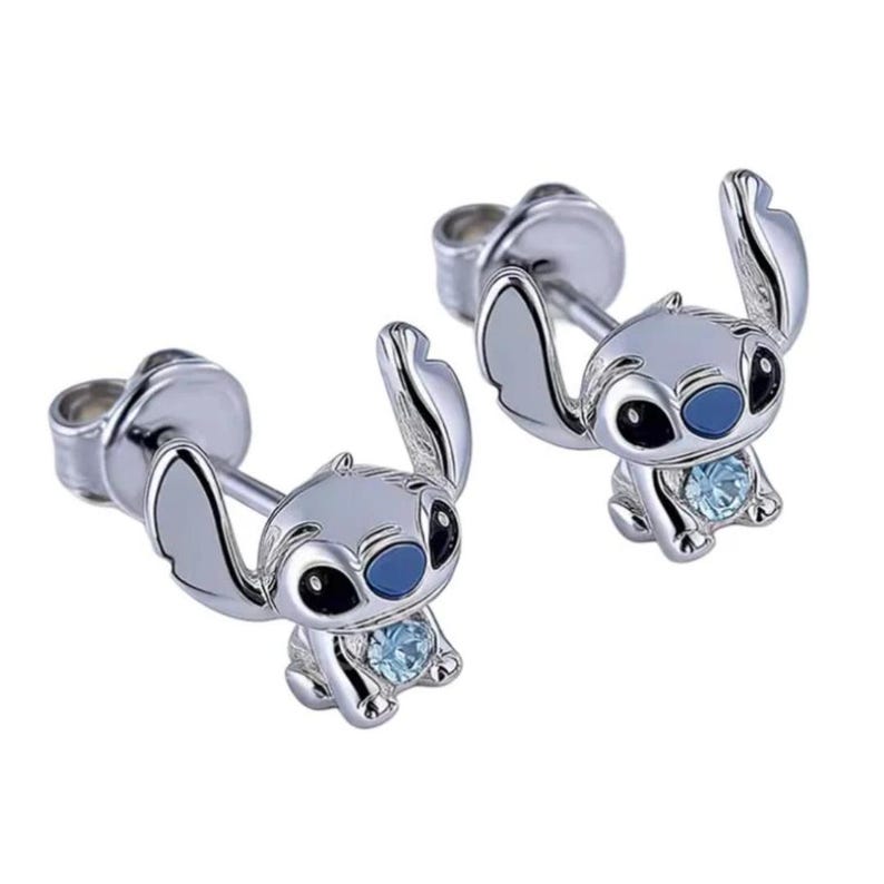 Puede incluir: Un par de pendientes de bot&oacute;n plateados con un dise&ntilde;o de personaje de dibujos animados. Cada pendiente representa una peque&ntilde;a criatura sentada con orejas grandes, ojos azules y una gema azul claro. Fondo blanco.