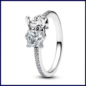 Puede incluir: Un anillo plateado con un peque&ntilde;o personaje de Stitch sosteniendo una gema cuadrada y transparente. La banda del anillo est&aacute; adornada con peque&ntilde;as gemas transparentes. El anillo est&aacute; sobre un fondo blanco.