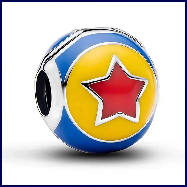 May include: A spherical metal charm bead featuring a vibrant enamel design. The surface displays a bright yellow circular center with a bold red five-pointed star, surrounded by a deep blue border. The metallic edges are polished and silver-toned.