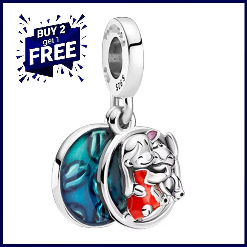 May include: A silver charm featuring a cartoon illustration of two characters hugging, with a blue and teal design on the reverse. The charm has a loop for attaching to a bracelet or necklace. The text "BUY 2 get 1 FREE" is in the upper left corner.