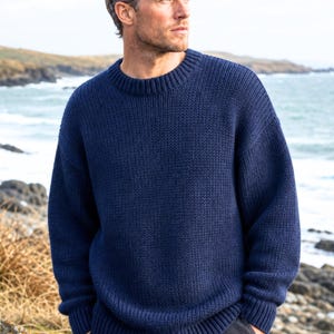 May include: A navy blue long-sleeve sweater featuring a thick, chunky knit texture, a round crew neckline, and ribbed detailing at the collar, cuffs, and hem. The garment is constructed with a relaxed fit and a solid, deep blue color throughout.
