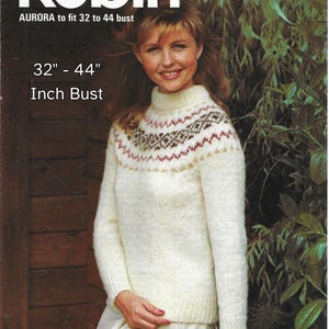May include: A woman wearing a cream-colored sweater with a high neck and patterned yoke. The sweater is part of a knitting pattern from Robin, designed to fit a 32 to 44 inch bust. The image includes the text "AURORA to fit 32 to 44 bust" and "Inch Bust".