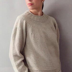 Puede incluir: Un suéter beige tejido con cuello redondo, puños y dobladillo acanalados. El suéter de manga larga tiene un diseño simple y clásico, y está hecho de un hilo suave y texturizado. El color neutro lo convierte en un básico versátil.