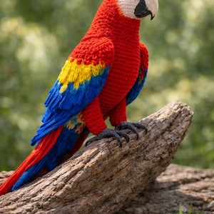Puede incluir: Un loro tejido a mano con colores vibrantes. El ave presenta un cuerpo rojo, alas amarillas y azules, y una cabeza blanca con un pico negro. Está posado sobre un trozo de madera, mostrando los intrincados detalles de la artesanía.