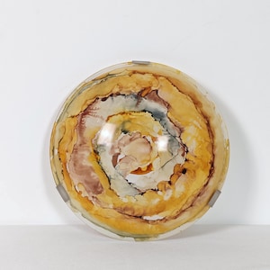 Könnte beinhalten: Dekorative Glasschale mit einem Wirbelmuster in Bernstein-, Braun- und Cremefarben. Die Schale hat eine kreisförmige Form und ist vor einem weißen Hintergrund platziert. Das Design ähnelt einem Geodenquerschnitt.