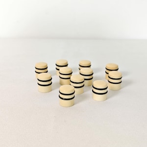 May include: A group of ivory-coloured, cylindrical objects, each featuring two black bands. They are arranged on a white surface. The design is simple and minimalist, suggesting a set of components or a product display.