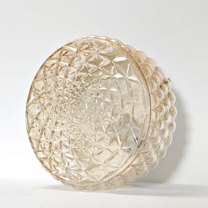 May include: A clear, round glass light fixture with a textured, geometric pattern. The fixture has a series of small, rounded bumps around the edge. The light fixture is a decorative element for home lighting.