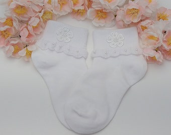 May include: A pair of white ankle socks with a delicate white flower embroidered on the top of each sock. The socks have a white lace trim with small white beads around the top.