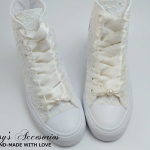 May include: A pair of white lace high-top sneakers with ivory satin ribbon laces and pearl accents.  The shoes are tied with a bow at the top.  "Rossy's Accesorios HAND-MADE WITH LOVE" is written on the bottom of the image.