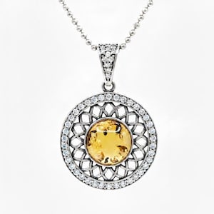 May include: Silver pendant necklace featuring a round, amber-colored stone at the center, surrounded by a decorative silver filigree and a halo of small, clear gemstones. The pendant hangs from a delicate silver chain.