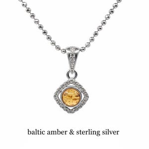 May include: A silver necklace with a pendant featuring a round, amber-colored stone set within a square frame of small, clear stones. The pendant hangs from a delicate ball chain. The text "baltic amber & sterling silver" is below the necklace.