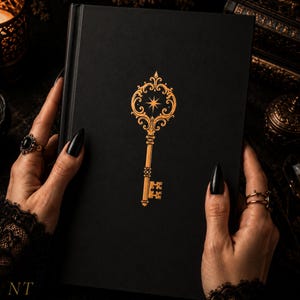 May include: A black hardcover book featuring a gold foil illustration of an ornate skeleton key centered on the front cover. The key design includes intricate scrollwork and a four-pointed star at the top, with a classic bit at the bottom.