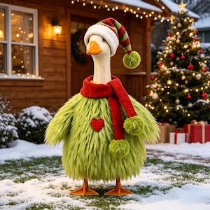 May include: A white goose wearing a fuzzy lime green sweater with a red heart patch, a long red scarf with green pom-poms, and a matching striped stocking cap with a green pom-pom. The goose has an orange beak and orange webbed feet.