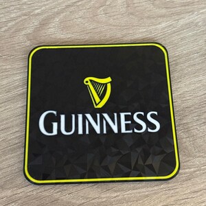 以下が含まれることがあります： 黒い正方形のコースターで、黄色の縁取りがあります。「Guinness」の文字が白で、その上に黄色のハープのロゴがあります。コースターの表面はテクスチャ加工されています。