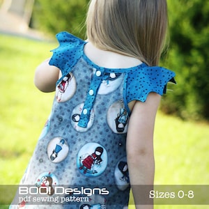 Op de afbeelding: Een blauw en grijs patroonjurk met een knoopsluiting aan de voorkant en vleermuismouwen. De jurk heeft een print van cirkelvormige illustraties met figuren. De tekst "BOO! Designs pdf sewing pattern" en "Sizes 0-8" zijn zichtbaar.